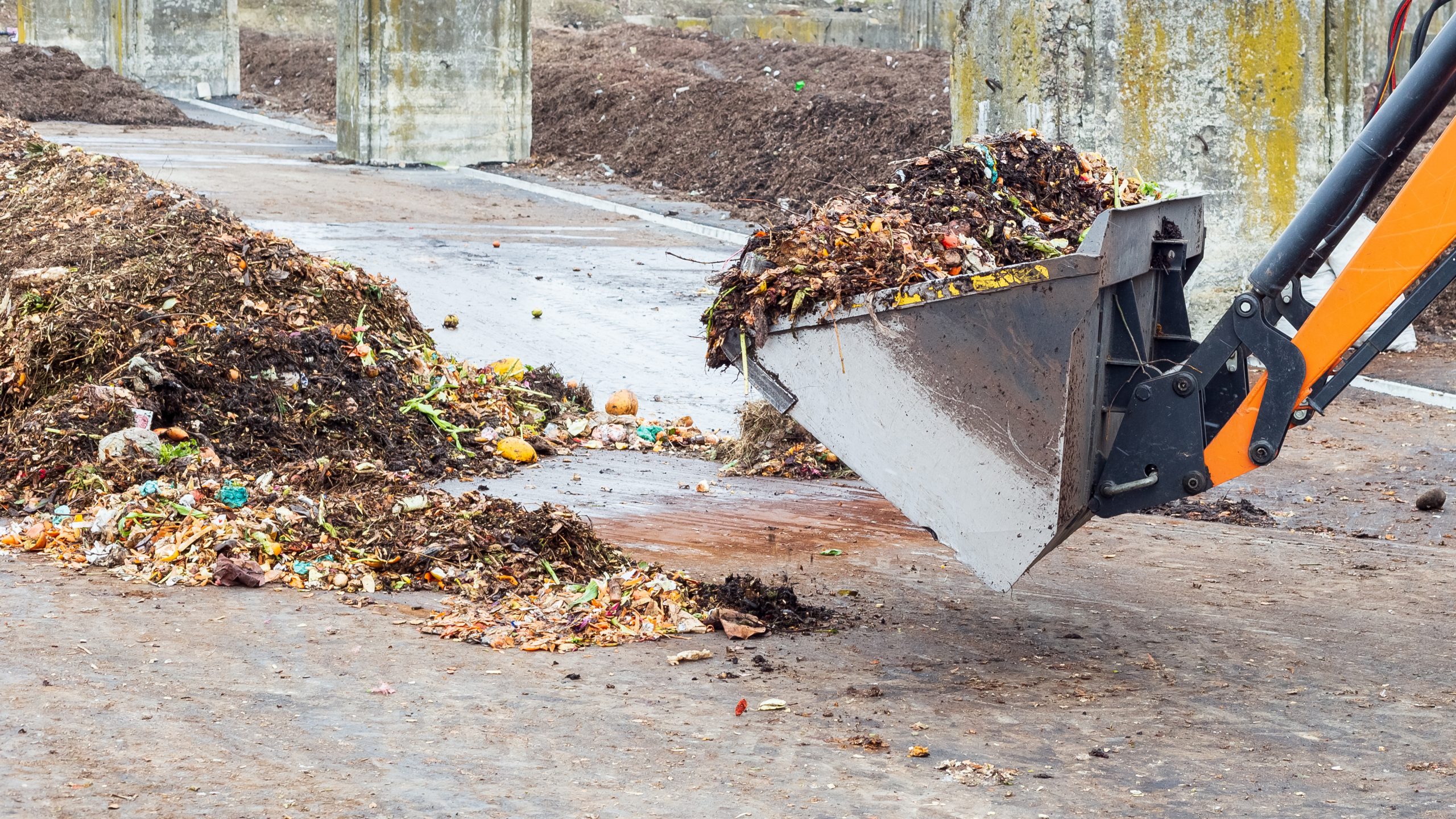 Industrial compost plant. Earth mover working with pile of compost in industrial facility. Turning organic waste to compost soil.